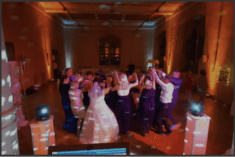 Eine Hochzeits-Partygemeinschaft tanz zusammen im Kreis. Einzelne Personen reißen die Arme in die Luft.