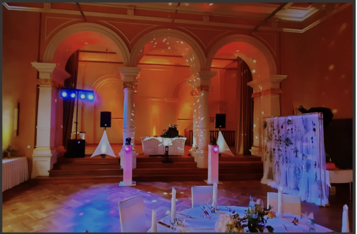 Eine Hochzeits-Location in warm-orangenem Licht. Im Vordergrund steht ein schön geschmückter runder Tisch.